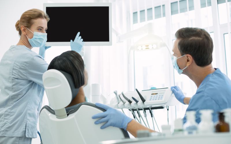 Man in a dentist chair with two dentist pointing at a screen