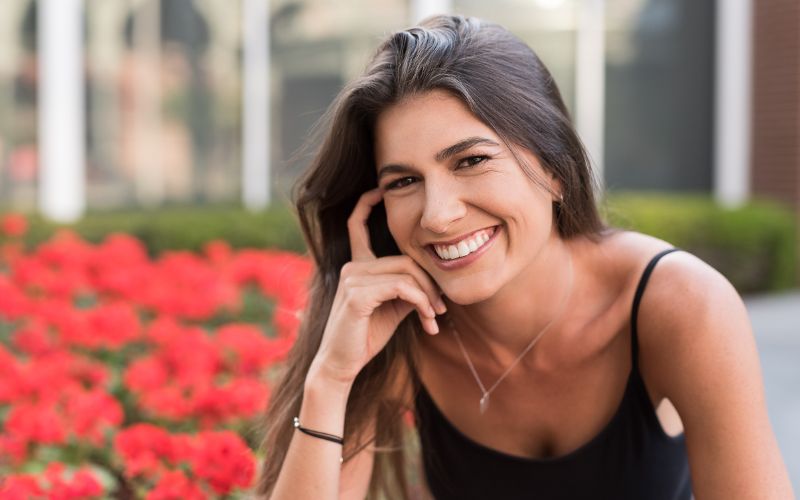 Young woman smiling with red flowers in the background.